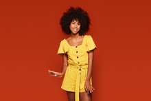 Vivid Carefree African American Woman In Bright Yellow Dress Standing On Red Background And Looking At Camera