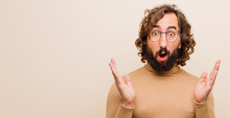 Canvas Print - young bearded crazy man looking shocked and astonished, with jaw dropped in surprise when realizing something unbelievable against flat color wall