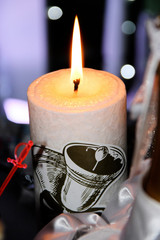 Burning white candle with flame and bells.