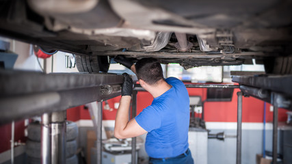 Wall Mural - Auto mechanic repairer checking condition under car on vehicle lift