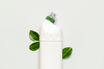 White plastic bottle for liquid detergent, cleaning agent, bleach, antibacterial gel with natural plant extract and green leaves on white background. Eco style cleaning concept. Flat lay top view