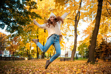 Happy Young Woman Jumping With Raised Arms On Colorful Autumn Leaves City Background