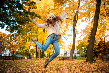 Happy young woman jumping with raised arms on colorful autumn leaves city background