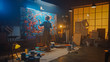 © Gorodenkoff - Talented Female Artist Working on a Modern Abstract Oil Painting, Gesturing with Broad Strokes Using Paint Brush. Dark Creative Studio Large Picture Stands on Easel Illuminated, Tools Everywhere