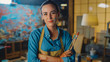 © Gorodenkoff - Young Female Artist Dirty with Paint, Wearing Apron, Crosses Arms while Holding Brushes, Looks at the Camera with a Smile. Authentic Creative Studio with Large Canvas. Head and Shoulders Portrait