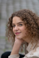 Close up of cheerful young woman with curly hair looking and smiling at the camera