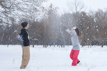 Loving couple having fun, laughing, playing and throwing snowballs in a winter park. A boyfriend and a girl friend spend winter time together.