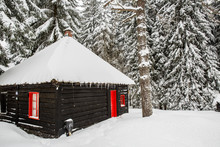 Black Wooden House With Red Door And Window On Snow