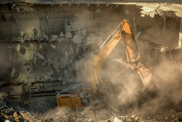 Heavy machinery surrounded with dust  cloud taking down an old building 