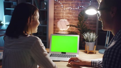 Office workers male and female are discussing business looking at green copy space laptop screen in workplace talking smiling. People and technology concept.
