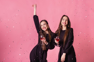 Two women celebrate the New Year party having fun laughing under the flying confetti and drinking wine.