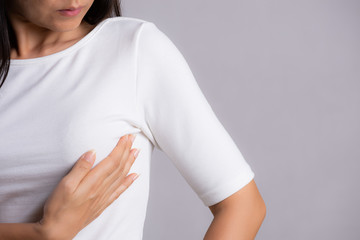 Woman hand checking lumps on her breast for signs of breast cancer on gray background. Healthcare concept.