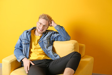 Sticker - Portrait of stylish young man sitting in armchair against color background