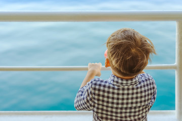 Asian boy stands on baluster of ferry for relaxing and look at the ocean and island