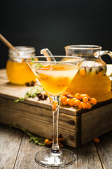 Hot autumn cocktail with sea buckthorn and orange juice in martini glass on the rustic background. Selective focus. Shallow depth of field.