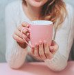 Pink Cup in the hands of a girl on a pink background.