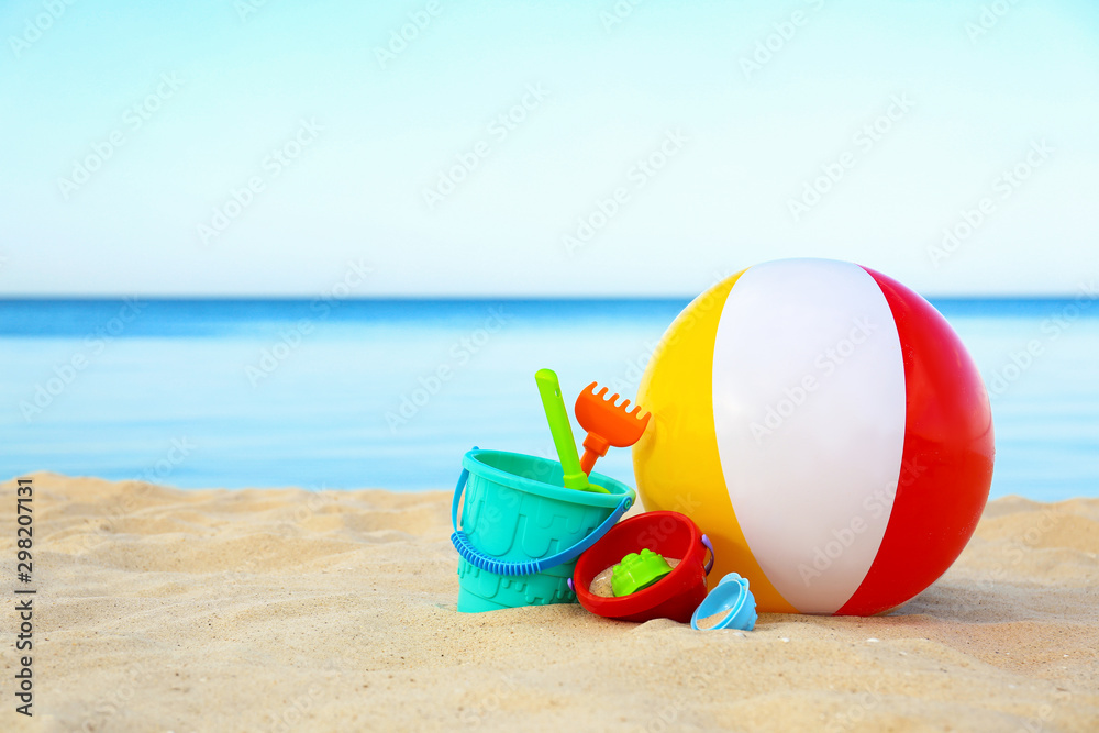 Set of plastic beach toys and colorful ball on sand near sea. Space for text - obrazy, fototapety, plakaty 