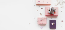 Banner With Holiday Presents. Gifts Wrapped In Pale Pink And Violet Paper With Silver Ribbons And Bow. Stars Confetti And White Copy Space. Top View, Flat Lay.