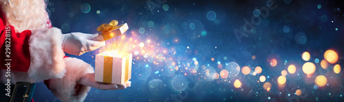 Fotografía Santa Claus Opening Christmas Present With Golden Stars In Night