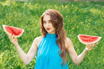 Portrait of pretty young woman holds two slices of watermelon. Beautiful brunette girl is holding two pieces of watermelon on grass background.