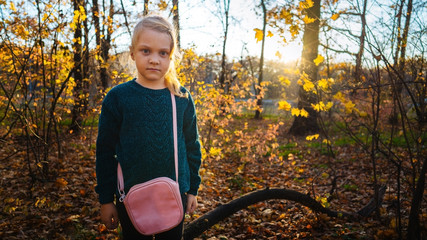 A charming little girl in a sweater is smiling on walk in autumn forest.