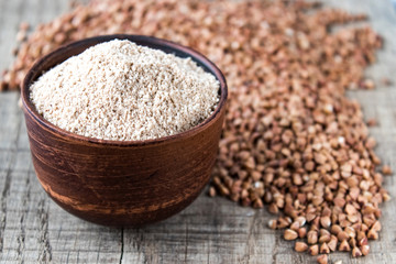 Wall Mural - Buckwheat flour in a bowl near the buckwheat grain. A pile of buckwheat flour.