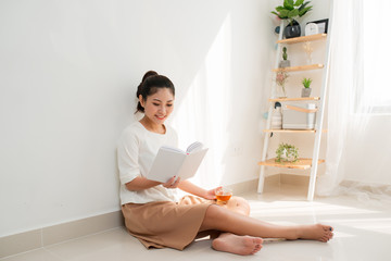 Pretty Asian woman drinking tea and reading book at home