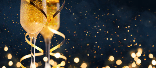 Two glasses of champagne with golden confetti, glitter, serpentine and lights.