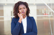 © Mangostar - Focused pensive leader thinking outside. Serious young black business woman standing at outdoor glass wall, touching chin and looking away into distance. Thinking concept