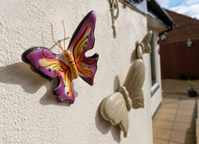 Ceramic Butterfly Ornaments Seen Attached To An Exterior Wall Of An Old House As Seen During Late Spring.