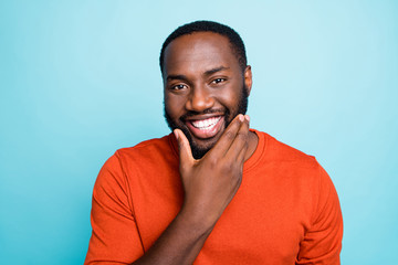 Closeup photo of attractive dark skin guy toothy beaming smiling touch cheekbones check beard growth temp wear orange pullover isolated blue color background