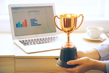 hand send trophy for achive person with background chart data on notebook screen which on the table 