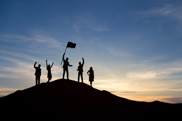 Wall Mural - Silhouette of people are celebrating success at the top of the mountain, sky and sun light background. Team business concept.