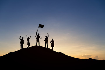 Wall Mural - Silhouette of people are celebrating success at the top of the mountain, sky and sun light background. Team business concept.