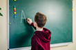 © Vadim - Student of higer school is standing in dark hoodie near the green blackboard in the classroom. Teenage Boy is writing alphabet on the board. School education concept.