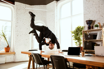 Young caucasian businessman having fun dancing break dance in the modern office at work time with gadgets. Management, freedom, professional occupation, alternative way of working. Loves his job.