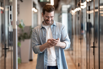 Wall Mural - smiling businessman using phone apps, standing in office hallway