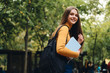 Pretty cheerful casual student girl with books happily looking in camera in park