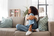 people, race, ethnicity and portrait concept - happy african american young woman sitting on sofa at home