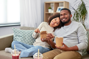 eating and people concept - happy african american couple with takeaway food and drinks at home