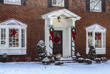 Entry And Porch To Traditional Georgian Style Brick House With Columns And Bay Windows Decorated For Christmas In The Snow