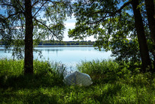 An Upside Down Boat In The Lush Green Grass Next To A Blue Lake On A Calm, Hot Summer Day In Snogeholm, Skåne, Sweden.
