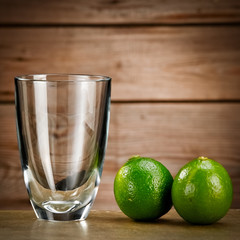 Empty glass and two limes on wooden background