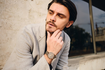 Portrait of young handsome man in coat thoughtfully looking away outdoor