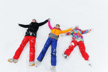 A Young Family Of Three-mom, Dad And Daughter Lie On The Snow In Brightly Colored Ski Suits Or In Winter Clothes And Make An Angel