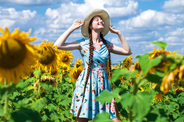 Young beautiful woman in a straw hat in a field of sunflowers