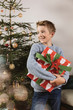 © Mareen Fischinger/Westend61 - Boy holding a large Christmas present in front of tree