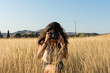 © Cavan Images - Young woman taking a picture with a camera in a meadow at sun