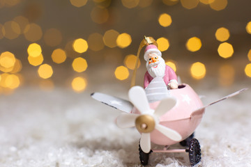 Decorative figurines of a Christmas theme. Santa Claus in a pink airplane with a propeller. Festive decor, warm bokeh lights.