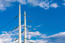 A Closeup View Of Two Transmission Poles For Overhead Power Lines, Against A Bright Blue Skyscape With Scattered Clouds And Room For Copy. City Electric Supply.